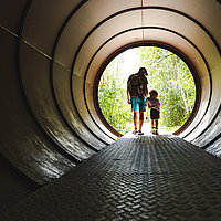 Ein Vater läuft mit seinem Kind durch eine Stahlröhre im Natur Park Südgelände