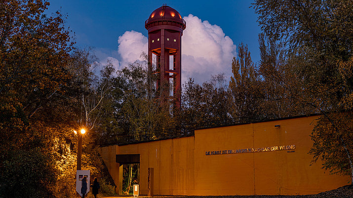 Der rote Wasserturm im Natur Park Südgelände hinter der gelben Wand