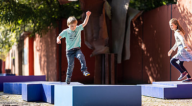 Kinder springen auf blauen Betonblöcken im Giardino Segreto herum