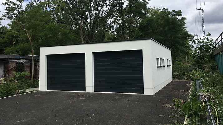 Eine Garage mit weißen Wänden und schwarzen Toren steht im Natur Park Südgelände an den Zuggleisen