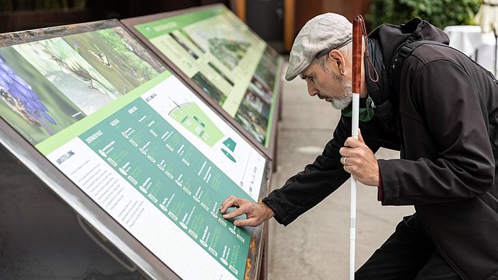 Ein Mann ertastet die barrierefreien Tasttafeln der Ausstellung "Bahnbrechende Natur" im Natur Park Südgelände