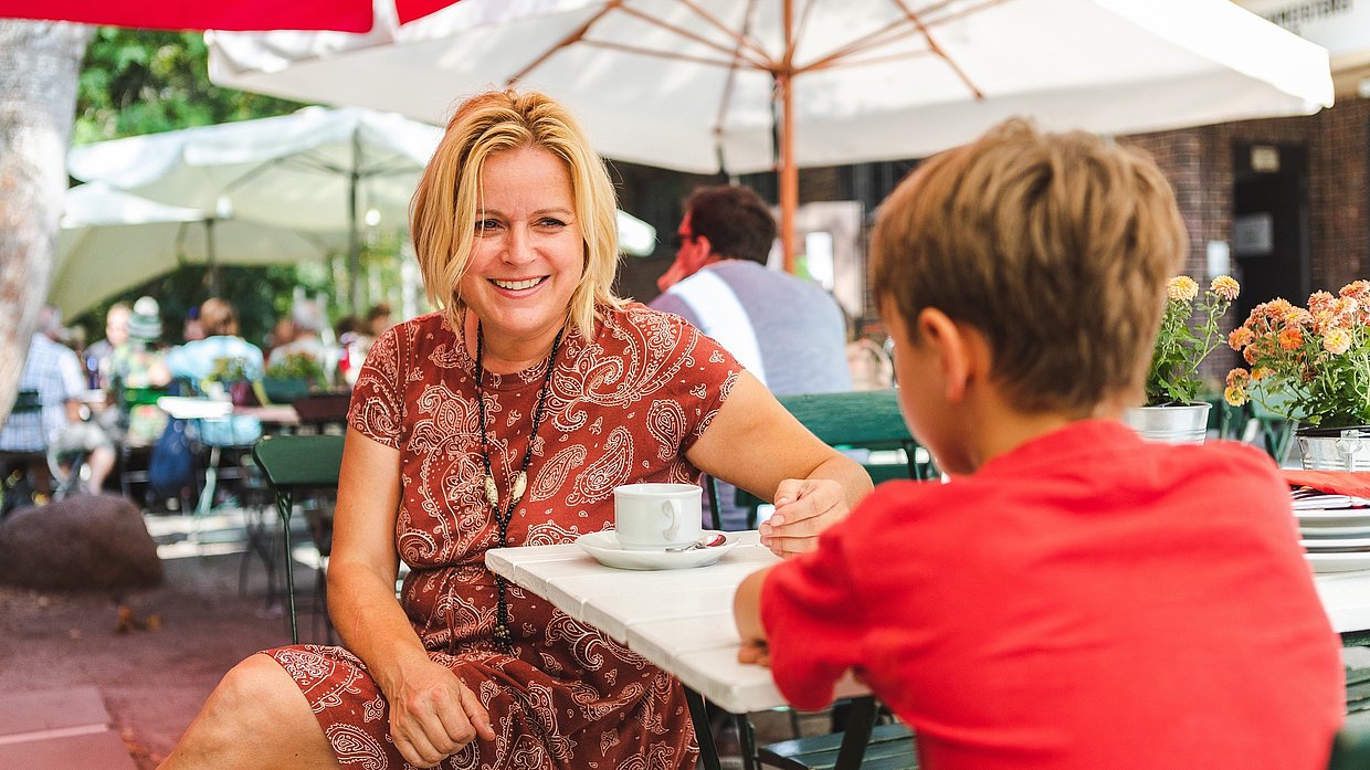 Eine Mutter sitzt mit ihrem Sohn auf der Terrasse des Café Paresüd im Natur Park Südgelände
